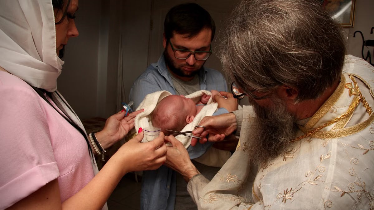 Intimate Ukrainian Orthodox baptism ceremony with priest, family, and newborn inside a church.