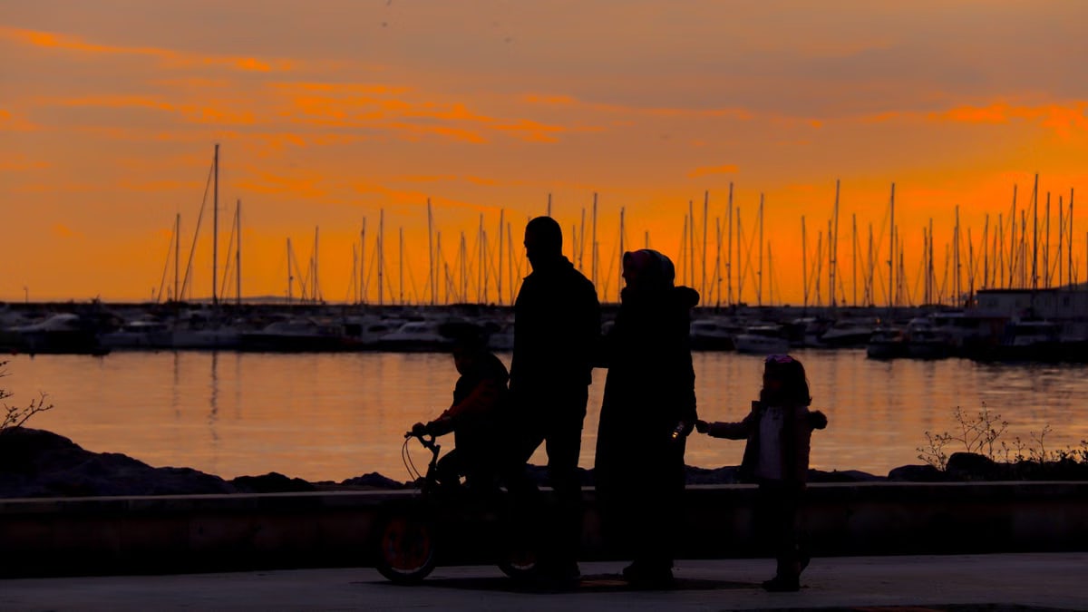 A silhouette of a family walking by the harbor at sunset with boats in the background.
